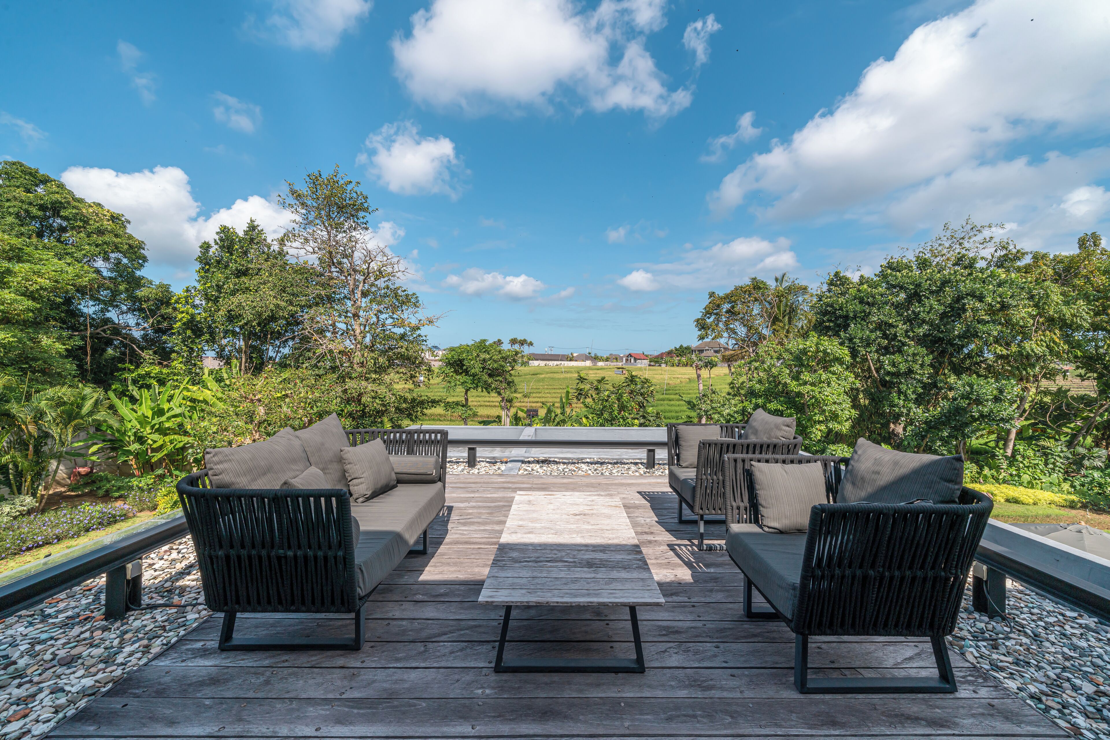 An outdoor patio with a sofa set and a coffee table, surrounded by a stone border and greenery.