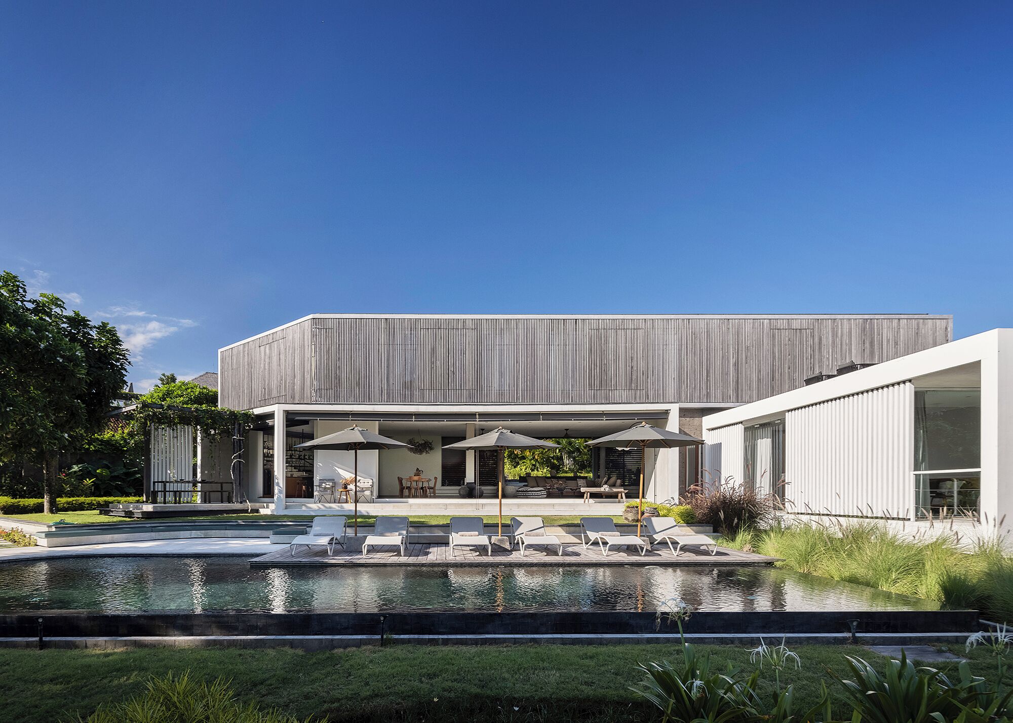 A modern building with a pool, outdoor seating, and a covered patio area.