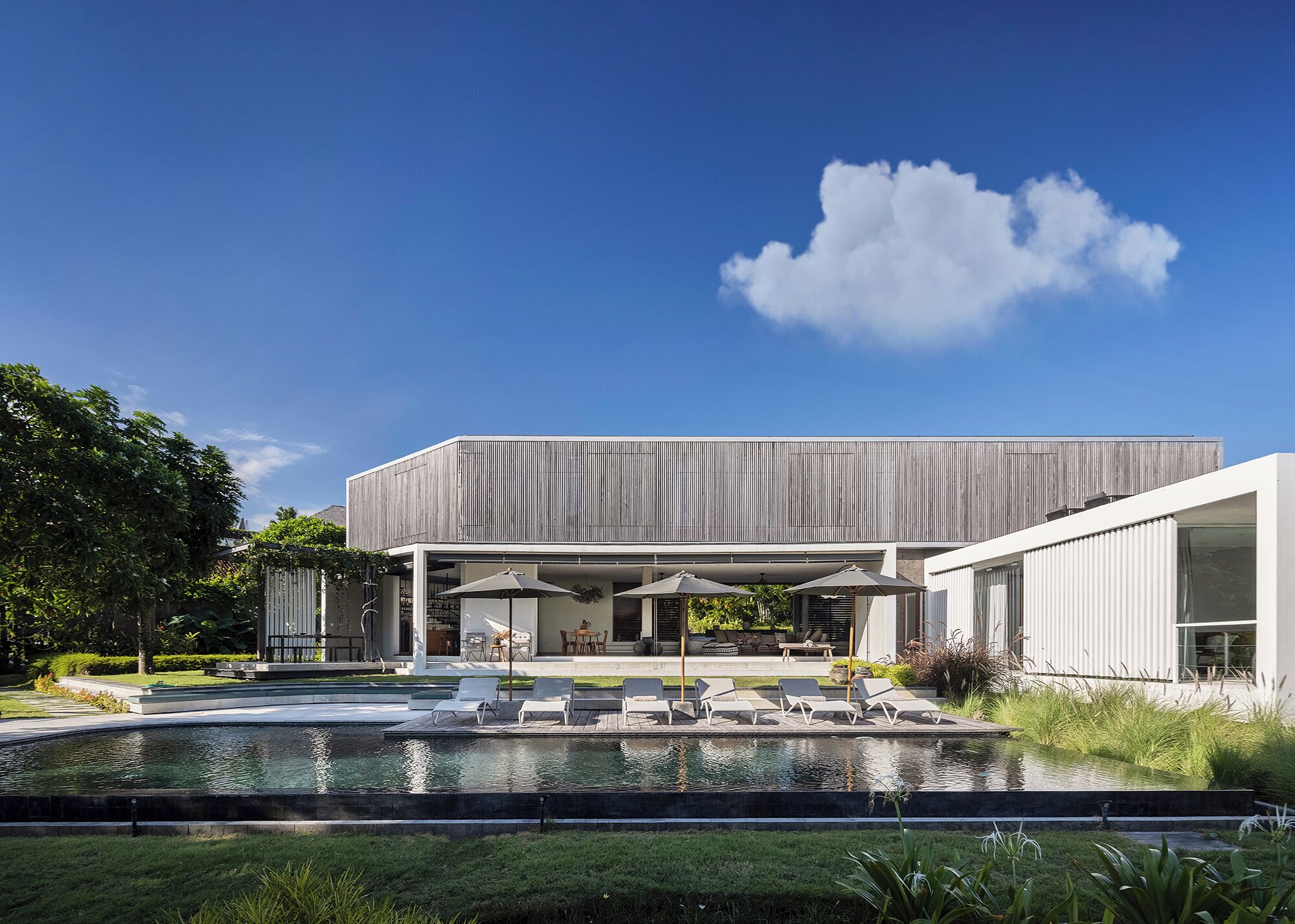 Une maison moderne dotée d’une piscine, d’un espace salon extérieur et d’un grand jardin.