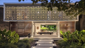 En moderne bygning med en geometrisk facade, en overdækket indgang og et veloplyst udendørs område med planter og siddepladser.