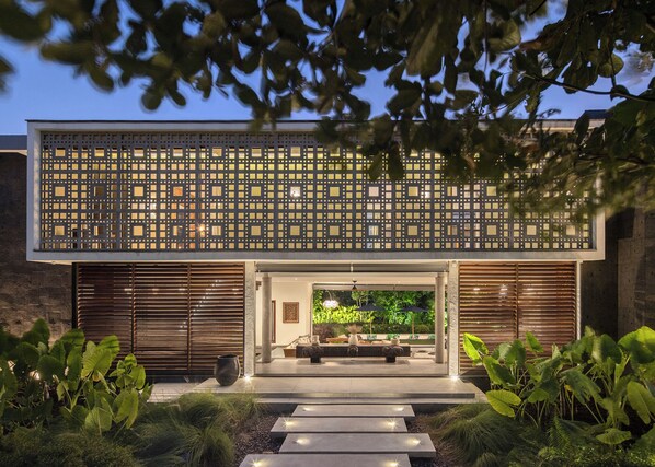 A modern building with a geometric facade, a covered entrance, and a well-lit outdoor area with plants and a seating area.