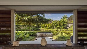A modern outdoor space with a stone bench, a decorative vase, and a view of a lush garden with a pathway leading to a building. - La Maison d'Ulysse  (Kerobokan)