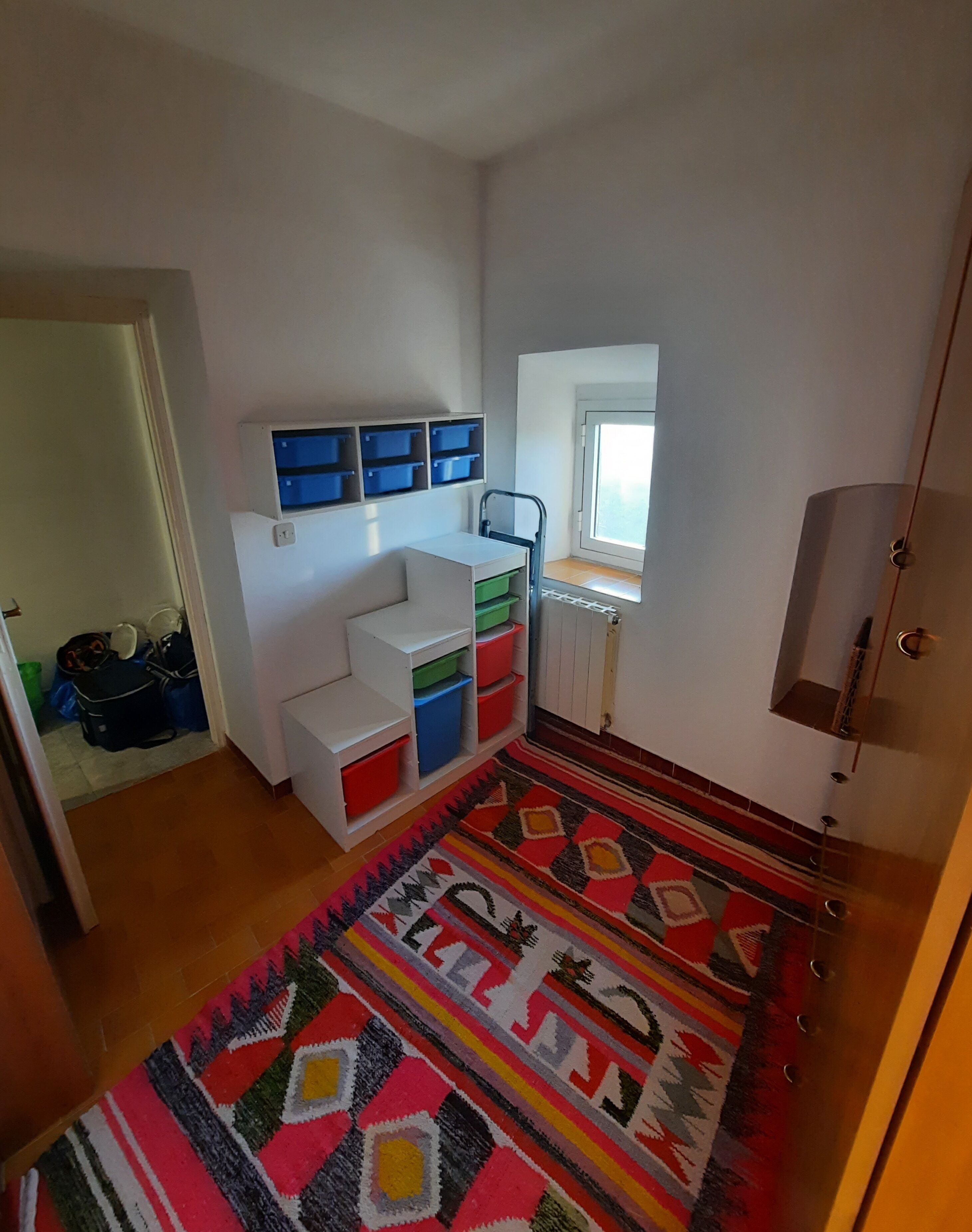 A room with a bed, a desk, a chair, a window, and storage units.