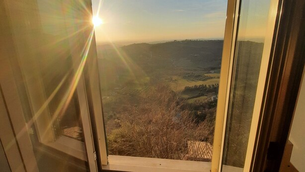 Une pièce dotée d’une grande porte vitrée donnant sur un balcon qui offre une vue sur un paysage vallonné.