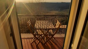 Un balcon offrant une vue sur un paysage lointain, une table en bois et une rambarde en métal.