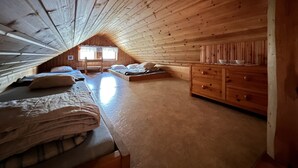 Quarto de sótão acolhedor, com ripas de madeira no teto, uma cama, um banco e uma cômoda.