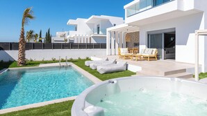 Un espace piscine extérieur moderne, doté d’un jacuzzi, de chaises longues et surplombé d’un ciel d’un bleu éclatant.