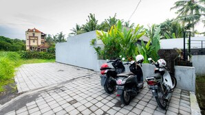 Dues motocicletes aparcades sobre una superfície pavimentada, amb una paret blanca i vegetació al fons.