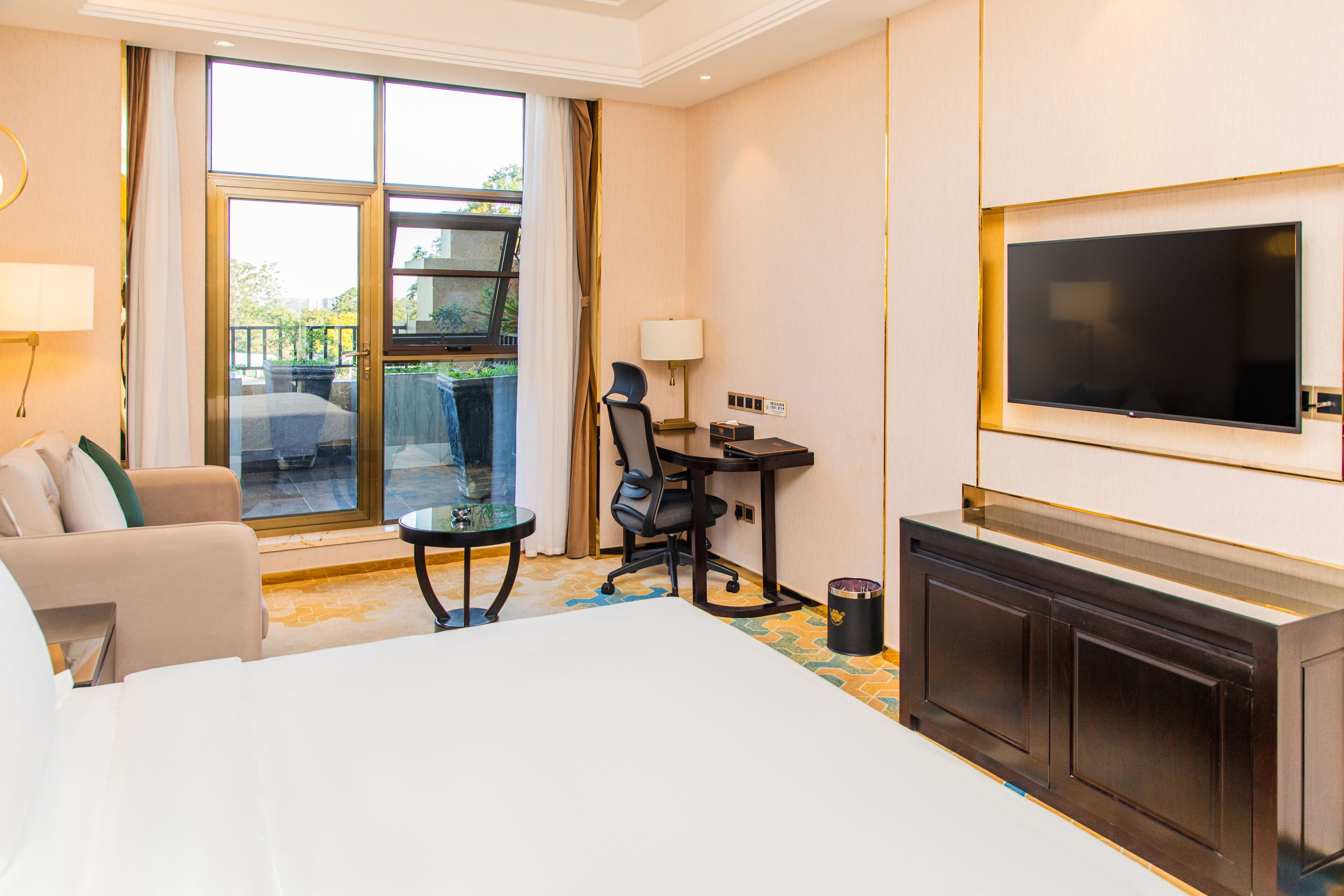 A hotel room with a bed, a desk, a chair, a TV, and a balcony with a view.