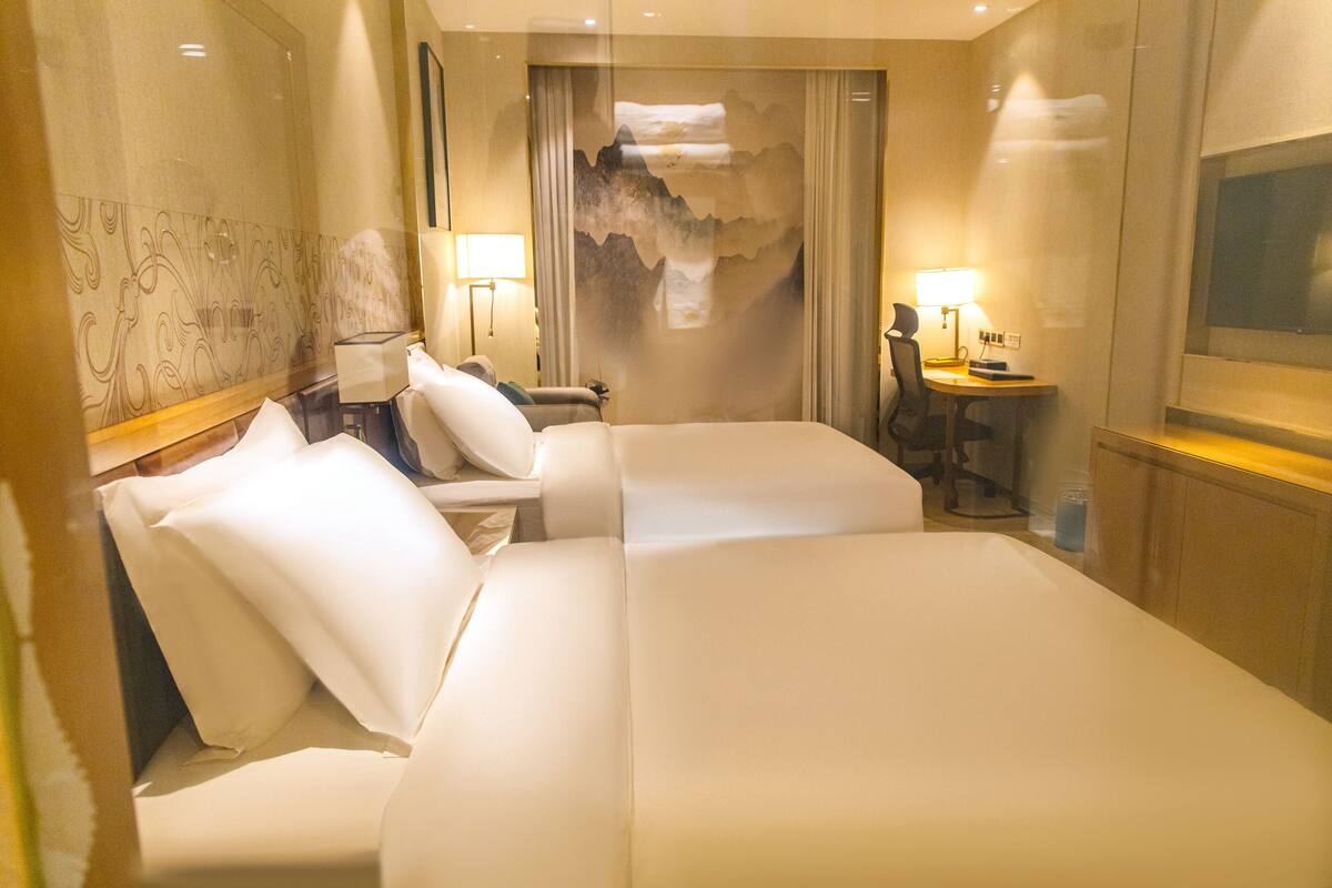 A hotel room with two beds, a desk, a chair, a lamp, and a large mirror.