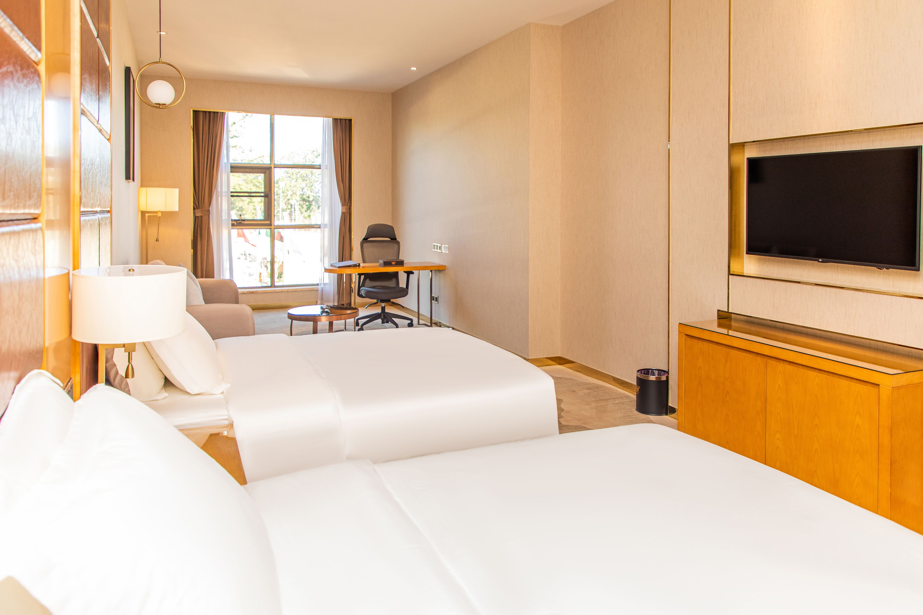 A hotel room with a large bed, a desk with a chair, a television, and a window with curtains.