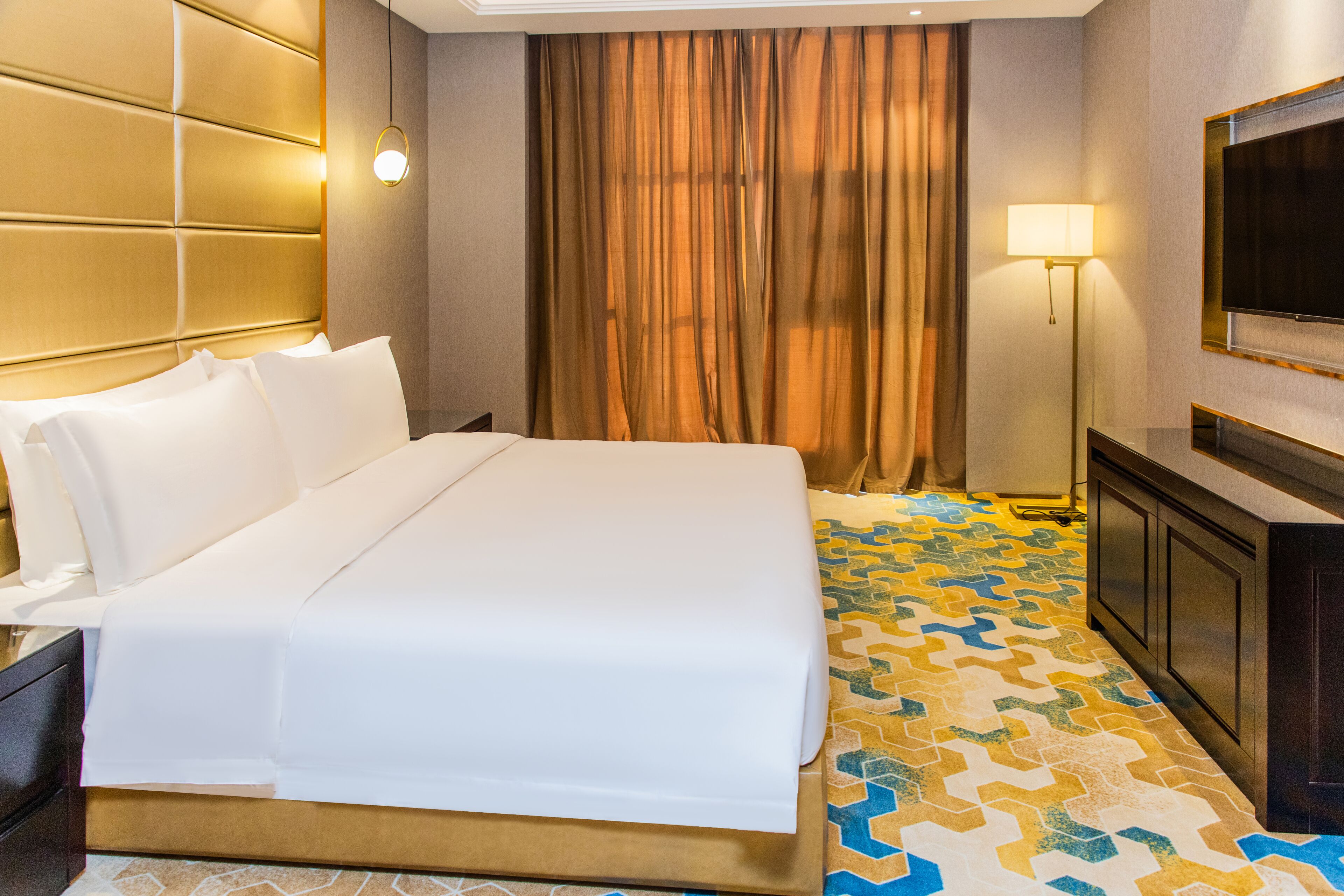 Habitación de hotel con una cama grande, un televisor en la pared, un escritorio con lámpara y un suelo con diseño.