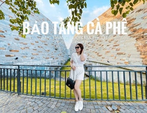A person standing in front of a modern building with a unique brick pattern and a metal fence. - Tru by Hilton Buon Ma Thuot City Centre (Buon Ma Thuot)