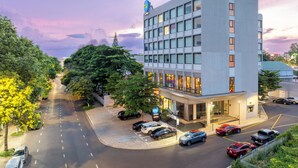 Een modern hotel met een vlakke gevel, meerdere verdiepingen en een parkeerplaats met auto's.