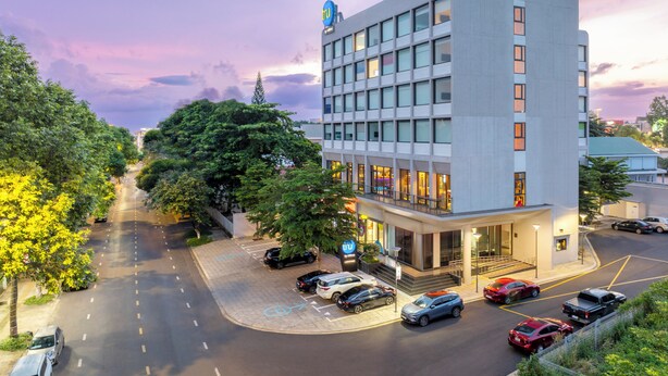 A modern hotel with a flat facade, multiple floors, and a parking area with cars.