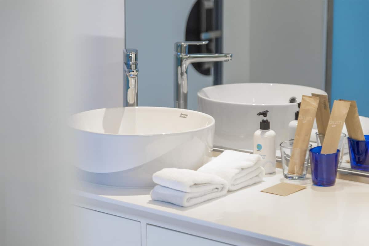 Une salle de bain avec un grand lavabo blanc, un miroir, un porte-serviettes et un verre d’eau.