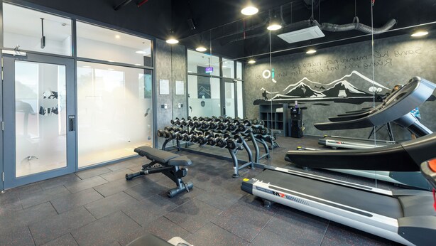 Een fitnessruimte met loopbanden, gewichten en een bank.