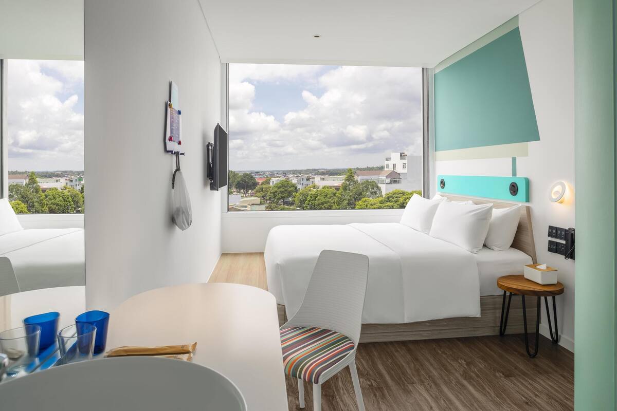 Ett modernt hotellrum med ett stort fönster, en säng, ett skrivbord och en stol.