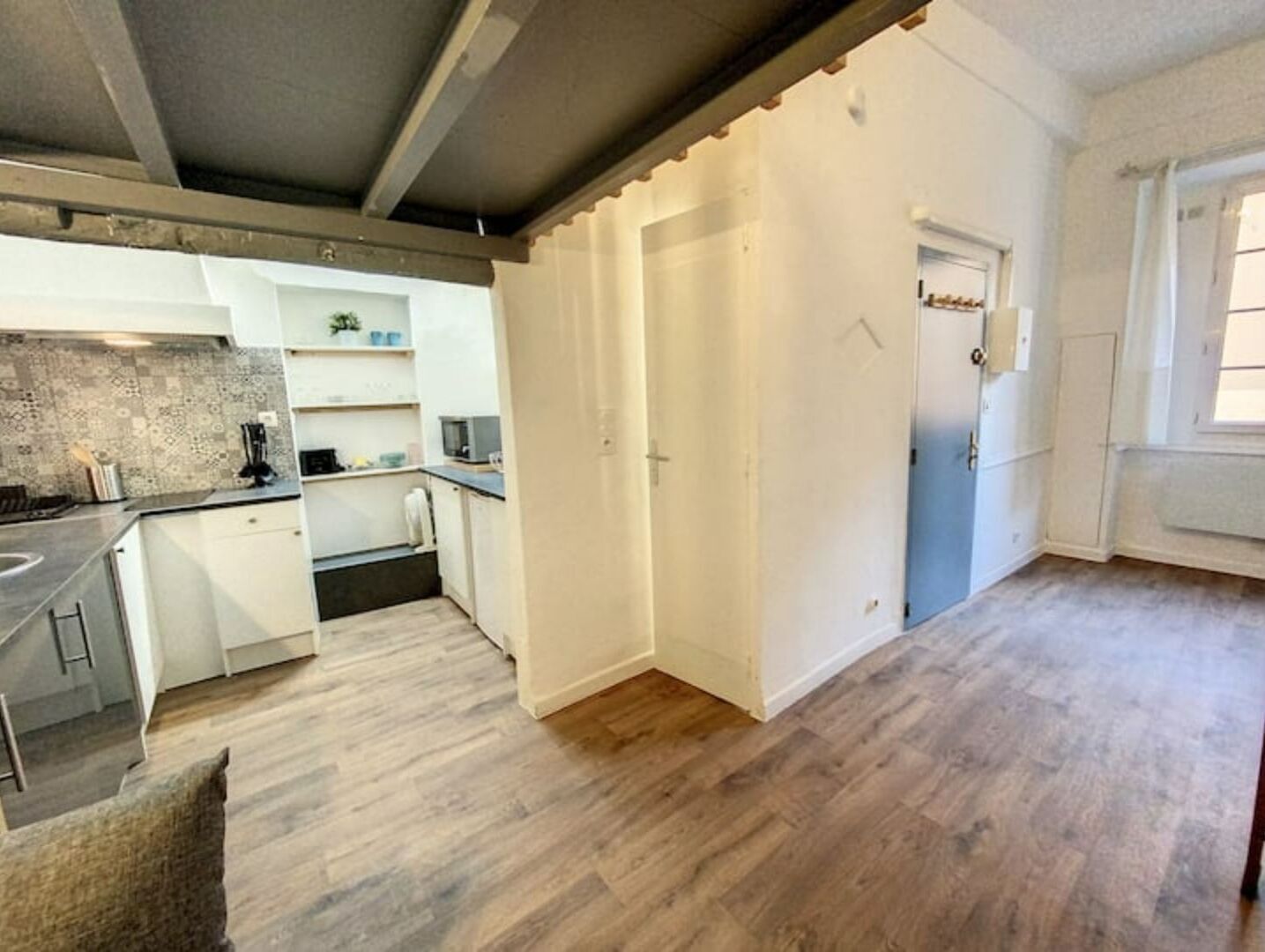 Cocina moderna con armarios blancos, microondas integrado y una pequeña isla. Hay una puerta que conduce a otra habitación y una ventana con cortinas.