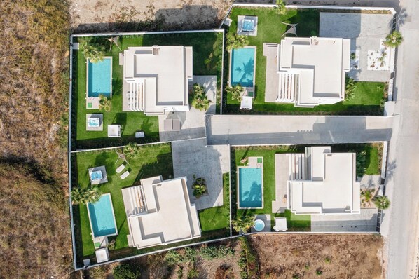 An aerial view of a residential property with multiple swimming pools, patios, and a well-maintained lawn.