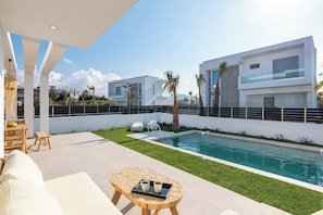 A modern outdoor pool area with a wooden table, lounge chairs, and a clear view of the pool.