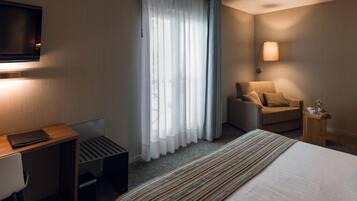 A hotel room with a bed, a desk, a chair, a TV, and a window with curtains.