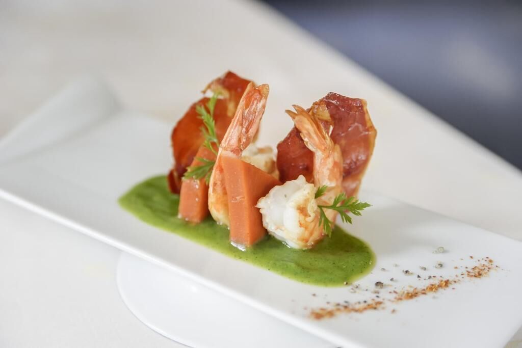 Un piatto con gamberi e prosciutto crudo, condito con salsa verde.