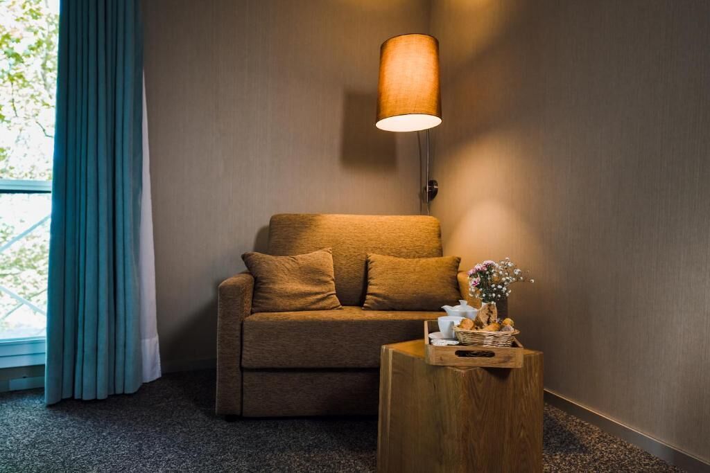 Una habitación acogedora con un sofá marrón, una mesita de madera con un jarrón de flores y una lámpara de pared.