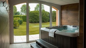 A hot tub in a room with a large sliding glass door leading to a garden. - Alysson Hôtel (Oloron-Sainte-Marie)