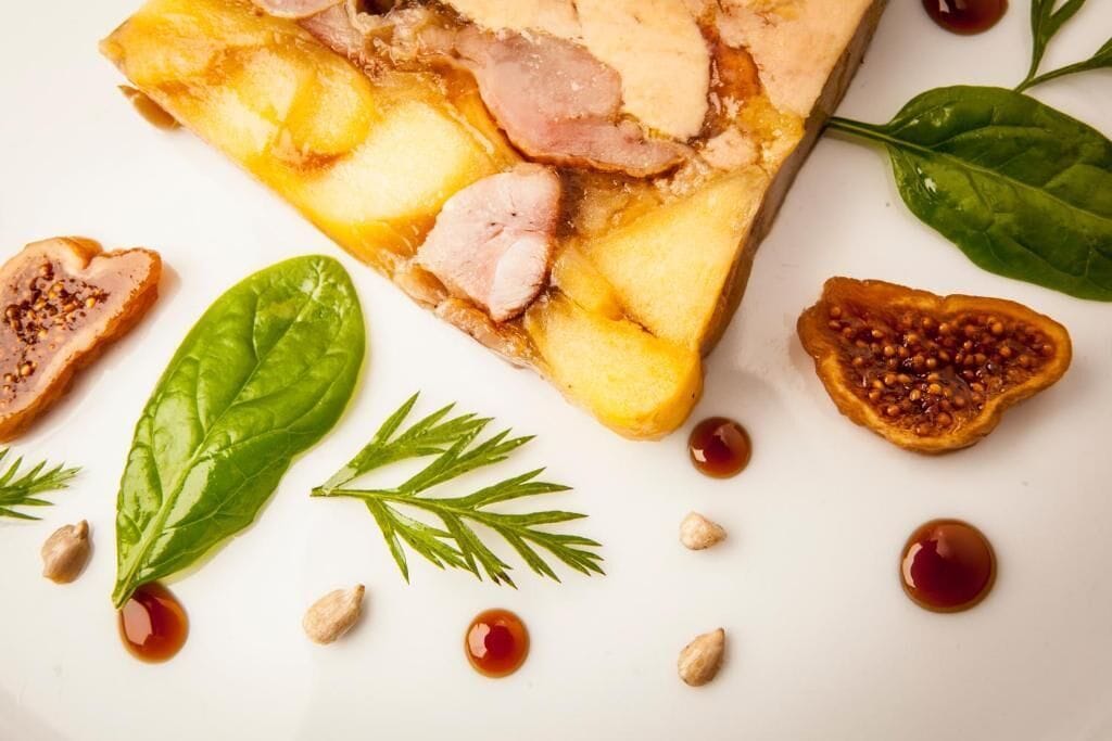 Una porción de pastel con carne y fruta, adornado con hojas de espinaca y nueces.