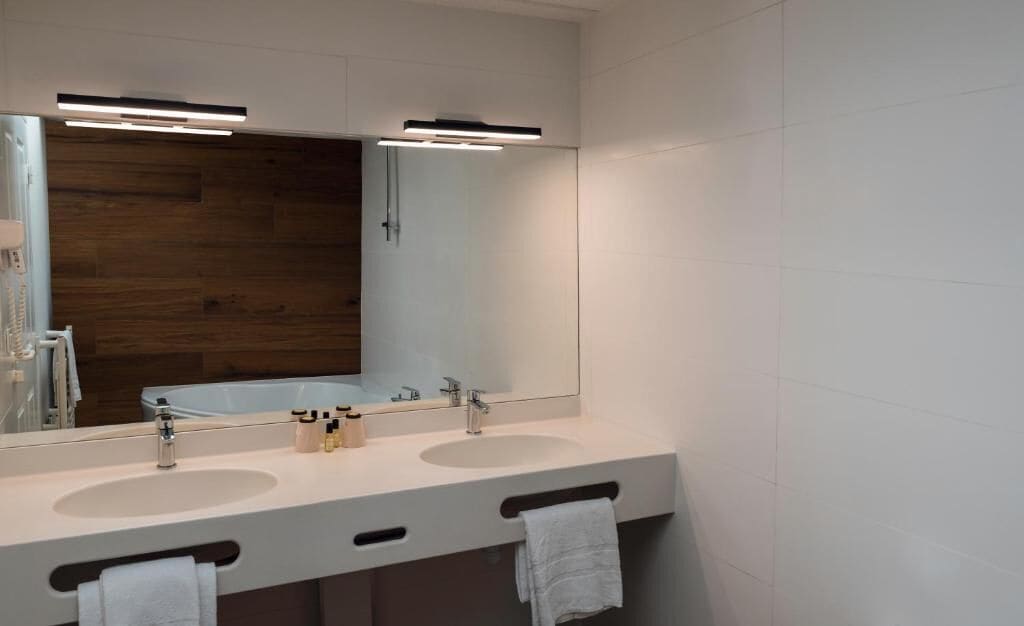 A modern bathroom with two sinks, a large mirror, and a wooden accent wall.