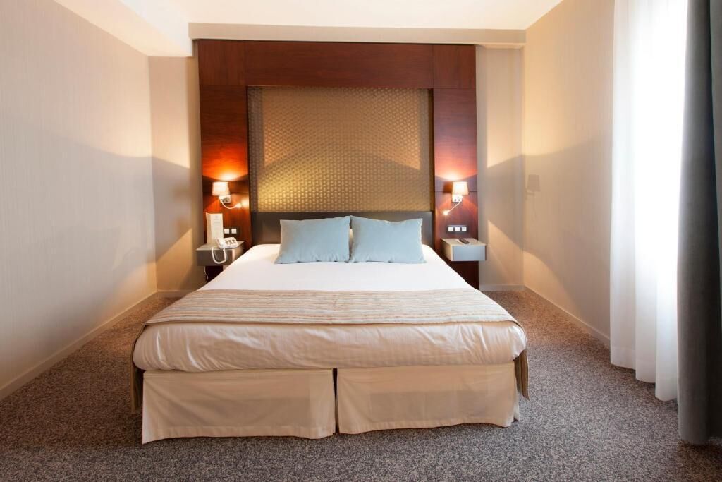 Una habitación de hotel con una cama grande, dos mesitas de noche y lámparas de pared.