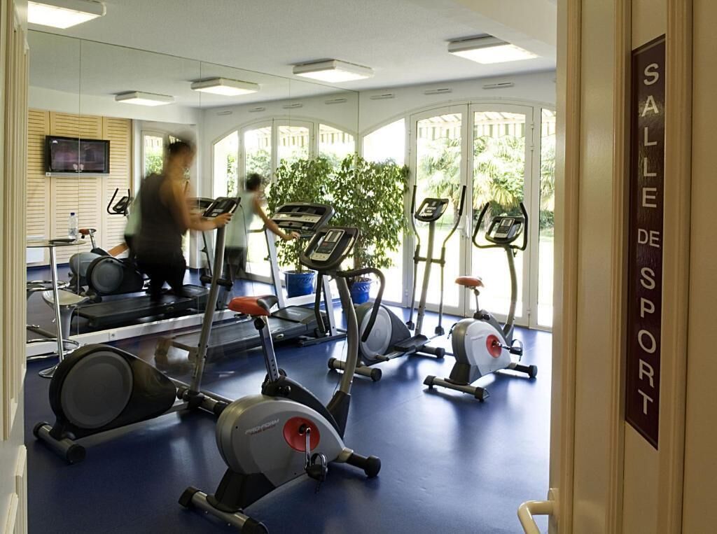 Un gimnasio con cintas de correr, bicicletas estáticas y un espejo grande.