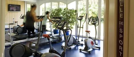 Un gimnasio con cintas de correr, bicicletas estáticas y un espejo grande.