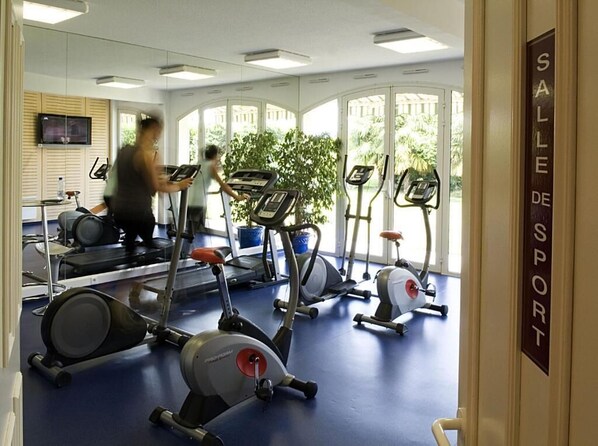 A gym with treadmills, stationary bikes, and a mirrored wall. - Alysson Hôtel (Oloron-Sainte-Marie)
