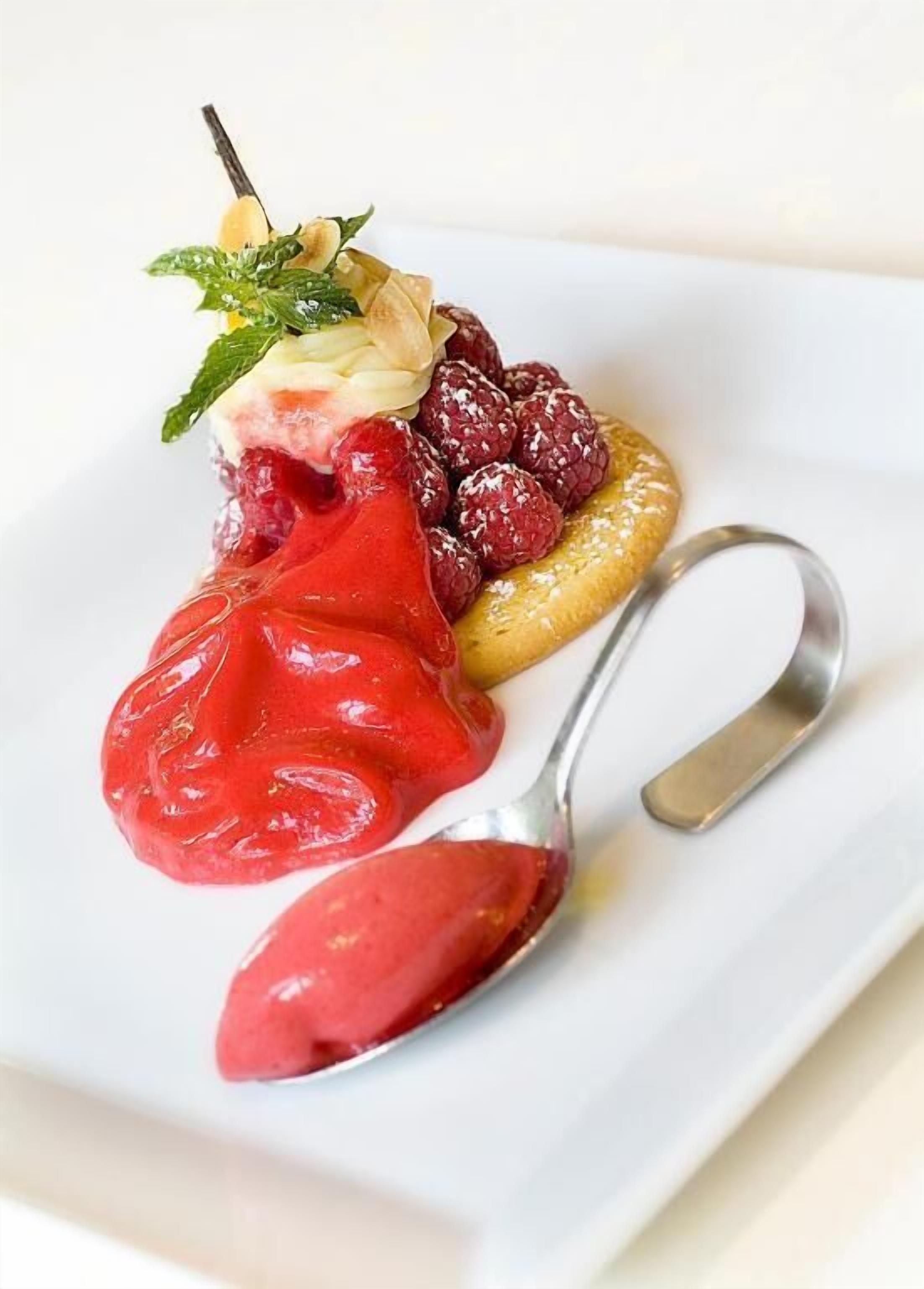 Un postre con una porción de helado rojo, frambuesas y hojas de menta sobre un plato.