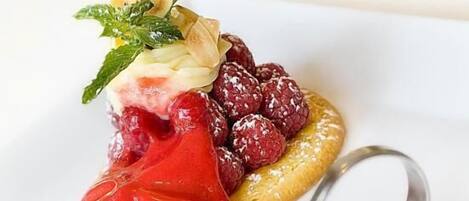 Un postre con una porción de helado rojo, frambuesas y hojas de menta sobre un plato.