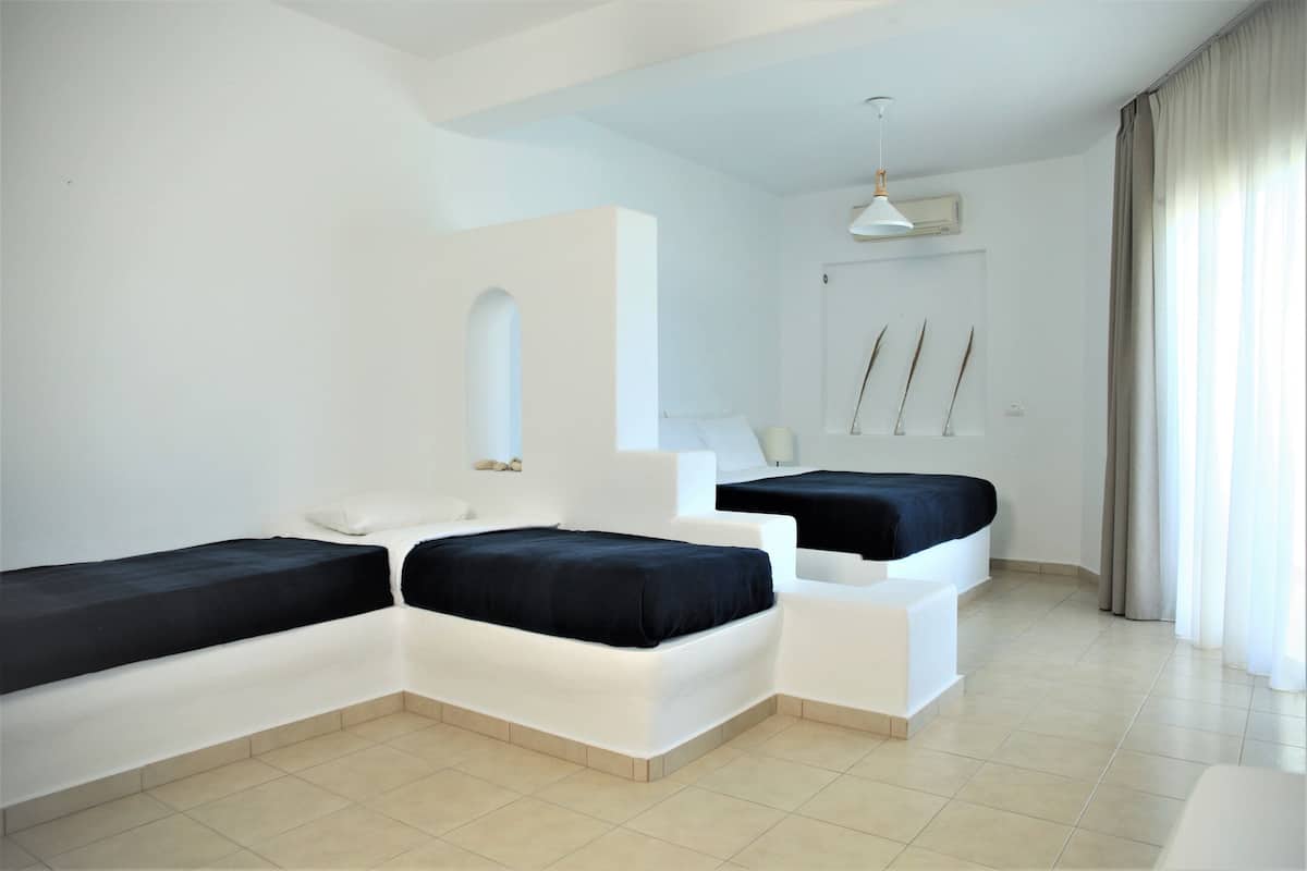 A modern hotel room with two beds, a large mirror, a ceiling fan, and a view of the beach.