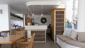 A modern interior with a wooden dining table, cushioned seating, pendant lighting, and a kitchen area with a stone wall. - Harmony Hotel (Sarandë)