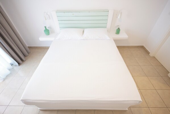 A bed with a white mattress and a green headboard in a room with a tiled floor and a white wall.