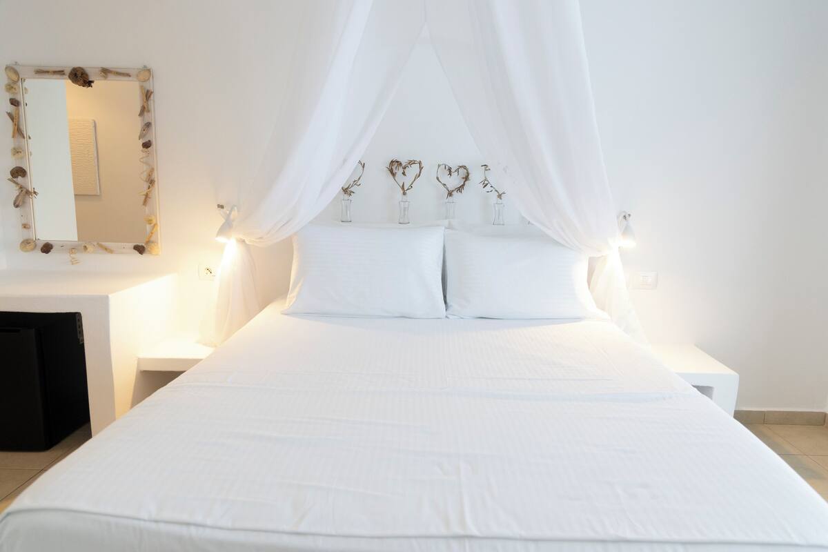 A bed with white bedding, a canopy, and heart-shaped decorations on the headboard.
