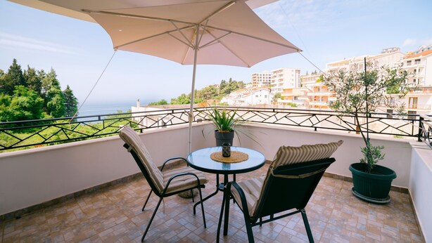 A balcony with a table and chairs, a potted plant, and a view of the sea and buildings. - Penthouse Lungo Mare Ulcinj (Ulcinj)