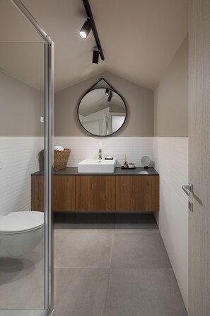 A modern bathroom with a wooden vanity, a round mirror, and a glass shower enclosure. - Modern apartment with hot tub (Poreč)