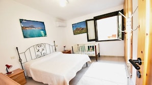 Une chambre à coucher comprenant un lit, un berceau, une table de chevet, une commode en bois, une fenêtre avec vue et des œuvres d’art murales.
