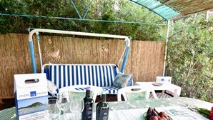 Un espace extérieur aménagé avec un canapé à rayures, une table à manger et des chaises, le tout entouré d’une clôture en bambou et de verdure.