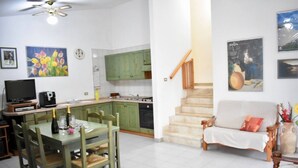 Un salon avec un canapé, une table à manger avec des chaises, un coin cuisine avec des meubles verts et un escalier.