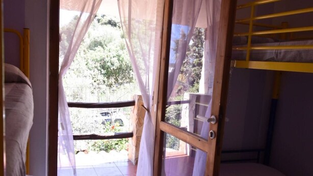 Una habitación con cama, ventana con cortinas traslúcidas y vista a zonas verdes.