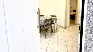 Un pasillo con una mesa de comedor y sillas, una puerta blanca y suelo de baldosas.