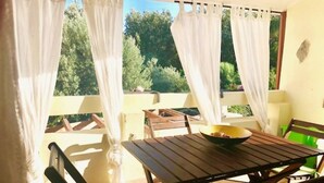 A balcony with a table and chairs, a bowl on the table, and white curtains.