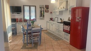 A kitchen with a dining table, chairs, a red refrigerator, and a window with curtains.
